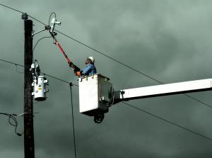 Image of lineworker in a bucket with an extendo stick changing out a fuse on an overhead line