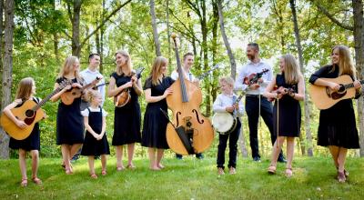 The Abello family standing at the edge of the woods looking at each other while holding their instruments.