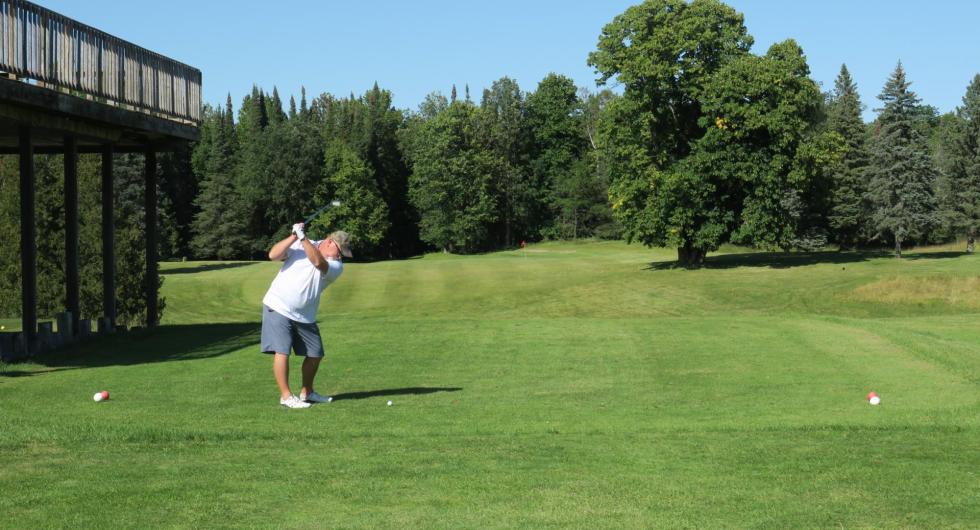 A golfer swings on the green in front of the clubhouse