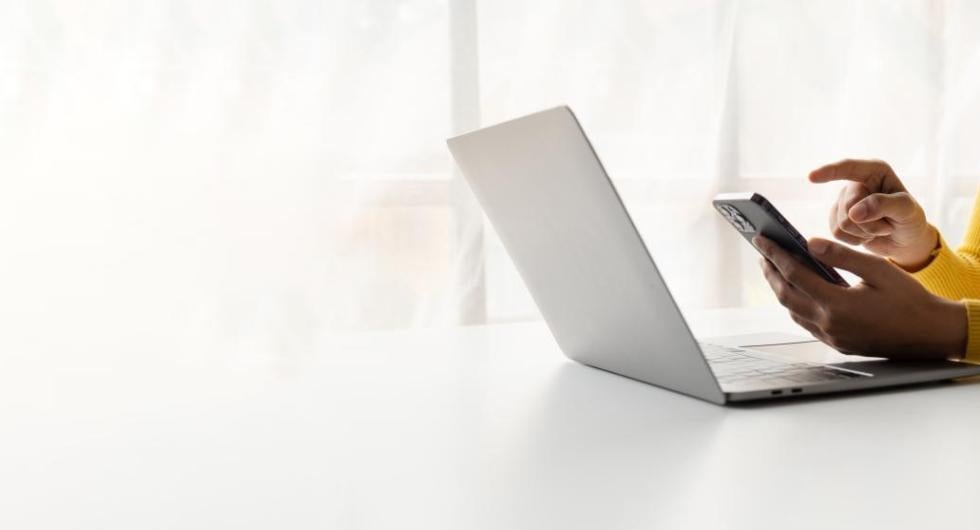 A woman holding a cell phone while also looking at laptop computer